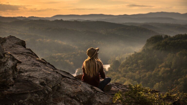 woman at top of mountain wearing a hat