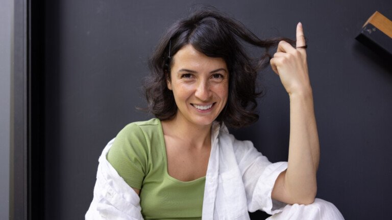 A woman sits against a plain background with hair curled around her finger to illustrate how understanding the hair growth cycle benefits hair regrowth expectations